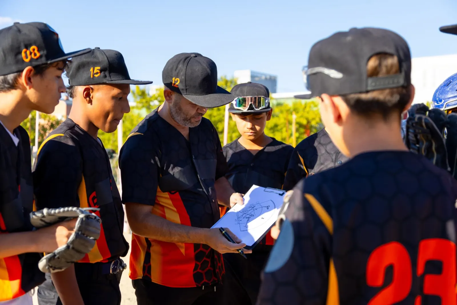 Baseball coach going over plays on a clipboard with a group of young players in a huddle